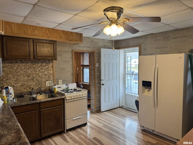 kitchen with dark brown cabinetry, sink, white appliances, light hardwood / wood-style floors, and a drop ceiling