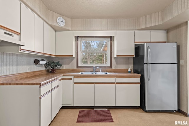 kitchen with white cabinets, sink, stainless steel fridge, and a textured ceiling