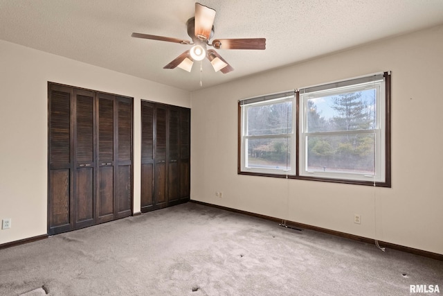 unfurnished bedroom with ceiling fan, a textured ceiling, light colored carpet, and multiple closets