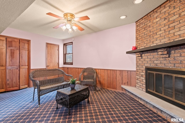 living room with wood walls, carpet, ceiling fan, a brick fireplace, and a textured ceiling