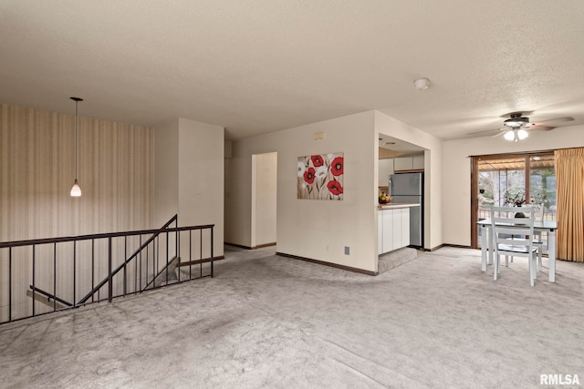 unfurnished living room with ceiling fan, light colored carpet, and a textured ceiling