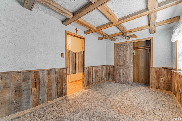 unfurnished bedroom featuring wooden walls, coffered ceiling, carpet, and beam ceiling