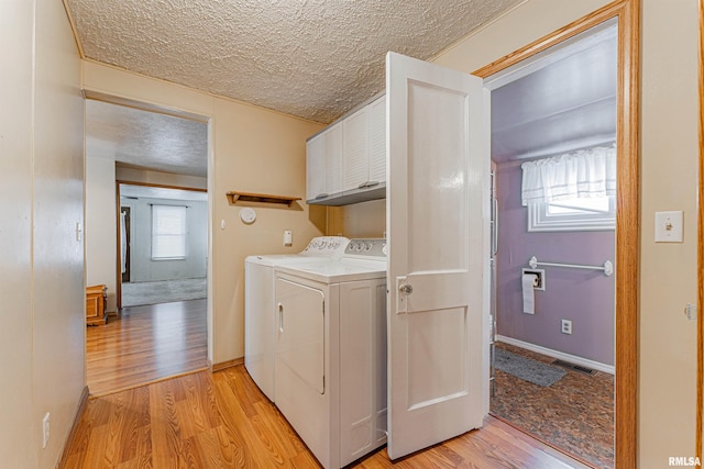 laundry area with cabinets, a healthy amount of sunlight, washing machine and clothes dryer, and light hardwood / wood-style flooring