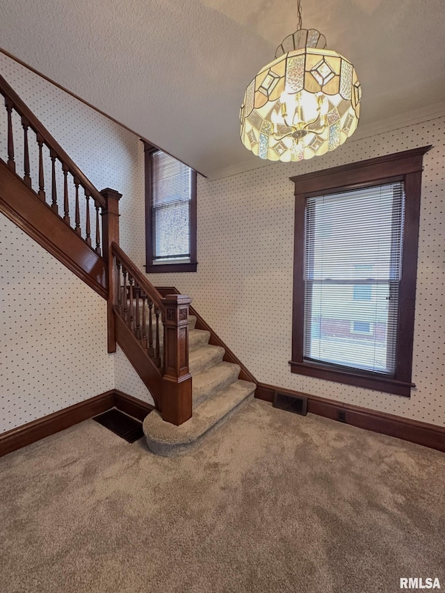 staircase with carpet floors, a notable chandelier, and a textured ceiling