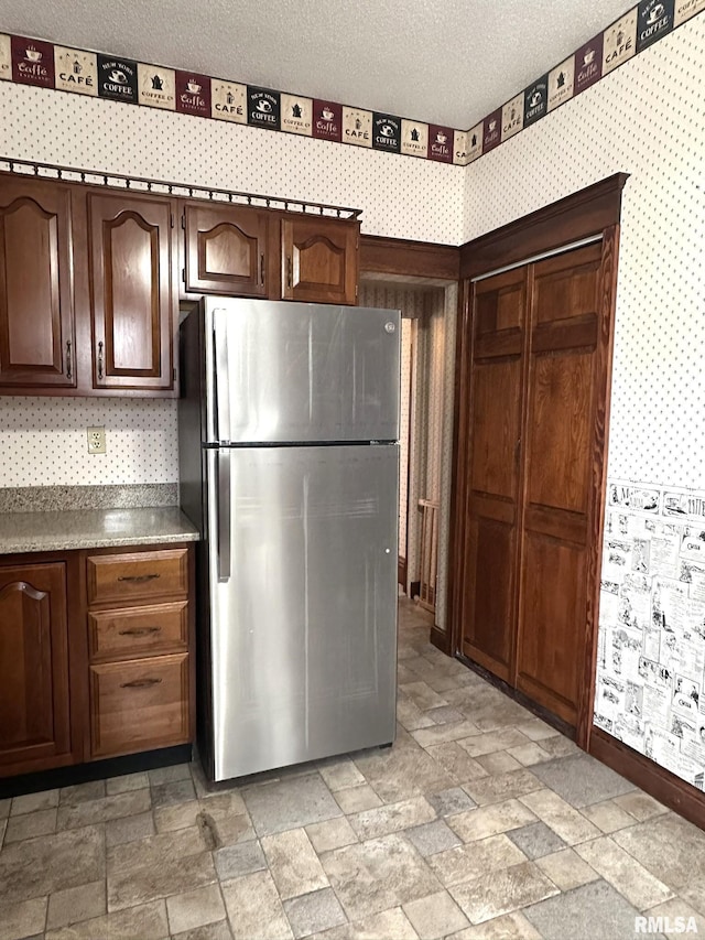 kitchen featuring stainless steel refrigerator, dark brown cabinetry, and a textured ceiling