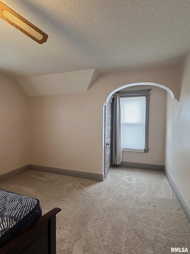 bedroom with ceiling fan, vaulted ceiling, light carpet, and a textured ceiling