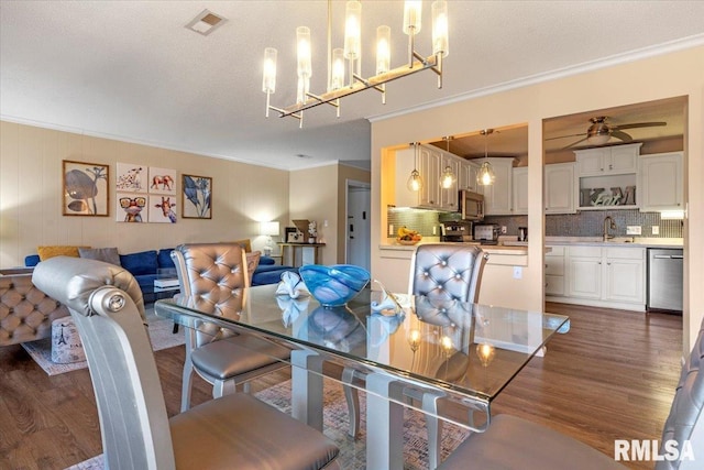 dining room with sink, crown molding, dark wood-type flooring, ceiling fan, and a textured ceiling