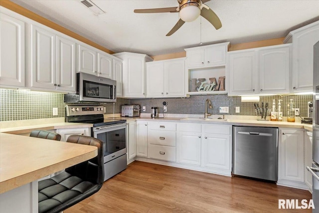 kitchen with appliances with stainless steel finishes, tasteful backsplash, white cabinetry, sink, and light wood-type flooring