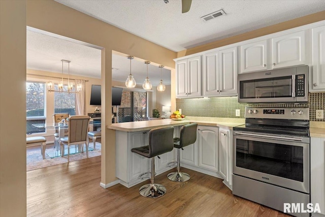 kitchen featuring pendant lighting, appliances with stainless steel finishes, white cabinetry, kitchen peninsula, and light wood-type flooring