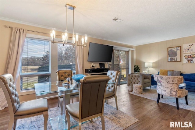 dining space featuring hardwood / wood-style floors, a notable chandelier, ornamental molding, and a textured ceiling