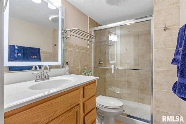 bathroom featuring vanity, toilet, a shower with shower door, and a textured ceiling