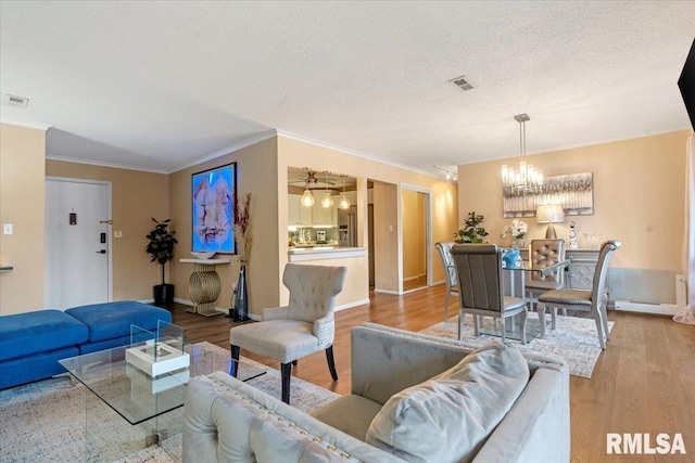 living room with crown molding, a chandelier, a textured ceiling, and light wood-type flooring