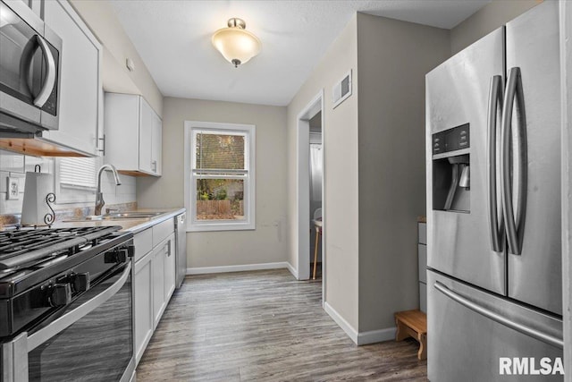 kitchen featuring sink, white cabinetry, light hardwood / wood-style flooring, stainless steel appliances, and decorative backsplash