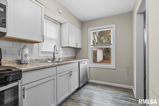 kitchen with sink, appliances with stainless steel finishes, light hardwood / wood-style floors, decorative backsplash, and white cabinets