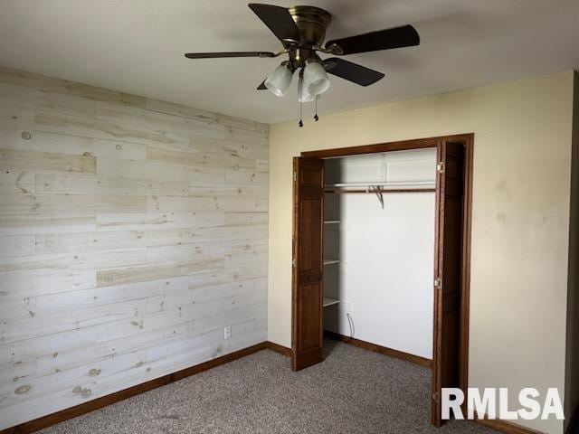 unfurnished bedroom featuring ceiling fan, carpet floors, wooden walls, and a closet