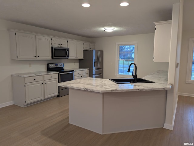 kitchen with sink, light wood-type flooring, kitchen peninsula, stainless steel appliances, and white cabinets