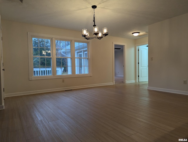 empty room with dark hardwood / wood-style flooring, a textured ceiling, and an inviting chandelier