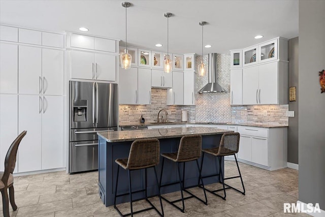 kitchen featuring white cabinets, a center island, stainless steel fridge, and wall chimney exhaust hood