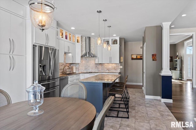 kitchen with wall chimney exhaust hood, a center island, appliances with stainless steel finishes, pendant lighting, and white cabinets