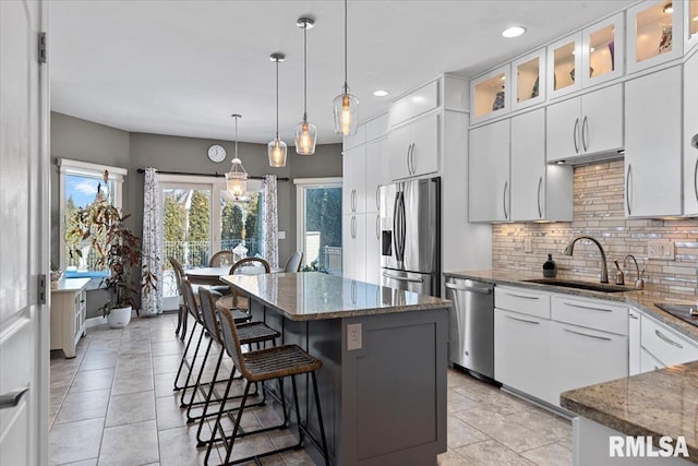 kitchen with sink, stone counters, white cabinetry, stainless steel appliances, and a center island