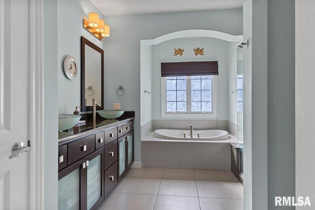 bathroom with a relaxing tiled tub, vanity, and tile patterned flooring