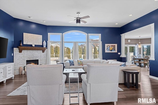 living room with dark hardwood / wood-style flooring, a stone fireplace, decorative columns, and ceiling fan