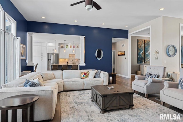 living room featuring wood-type flooring, decorative columns, and ceiling fan