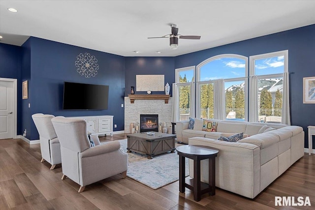 living room with ceiling fan, a stone fireplace, and hardwood / wood-style floors