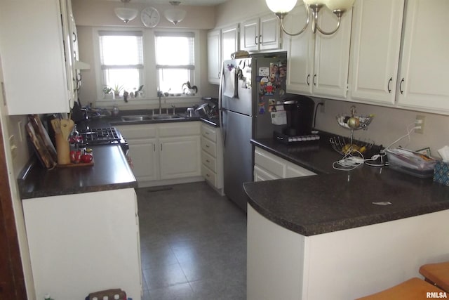 kitchen with white cabinets, a peninsula, a sink, dark countertops, and freestanding refrigerator