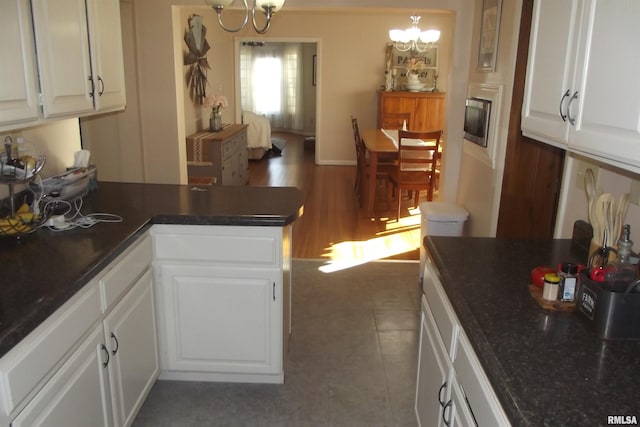 kitchen with dark countertops, white cabinets, a chandelier, stainless steel microwave, and a peninsula