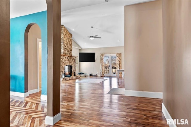 living room featuring baseboards, ceiling fan, wood finished floors, a stone fireplace, and high vaulted ceiling