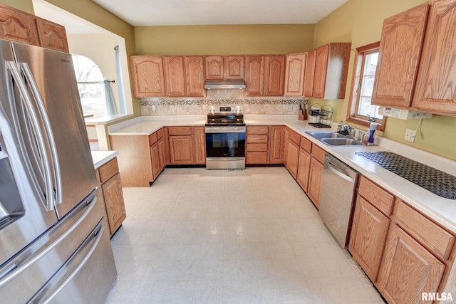 kitchen featuring stainless steel appliances, tasteful backsplash, light countertops, a sink, and under cabinet range hood