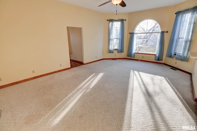 empty room featuring a wealth of natural light, visible vents, ceiling fan, and baseboards