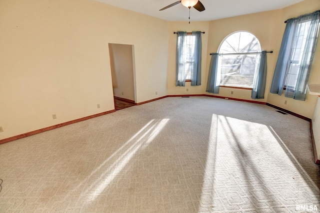 carpeted empty room featuring a ceiling fan, visible vents, plenty of natural light, and baseboards