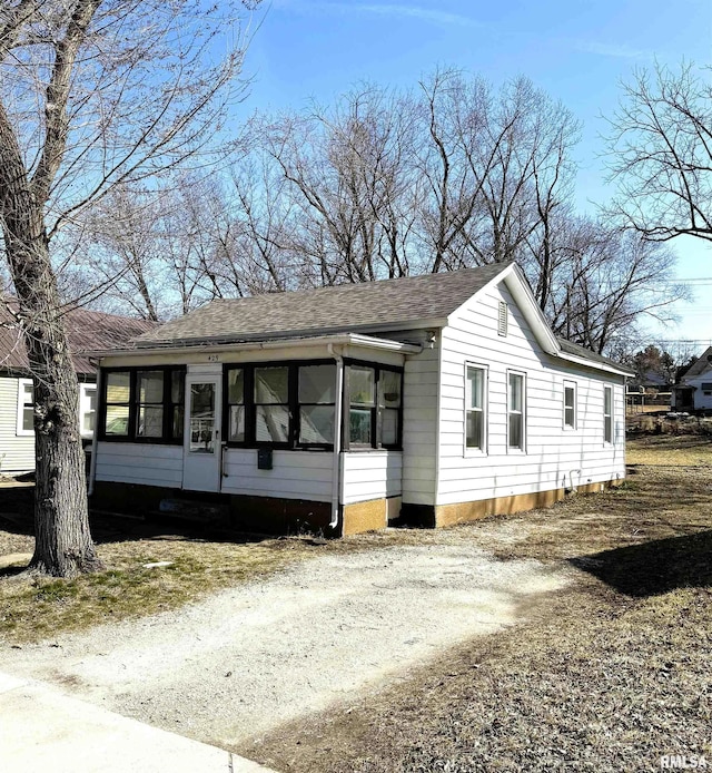 view of front facade featuring dirt driveway, roof with shingles, and a sunroom