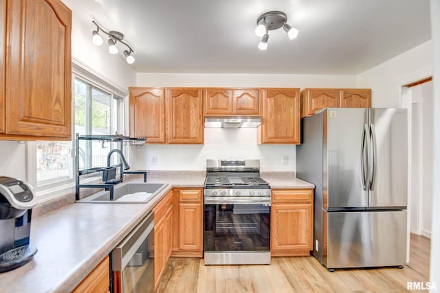 kitchen with light wood-type flooring, light countertops, under cabinet range hood, a sink, and appliances with stainless steel finishes