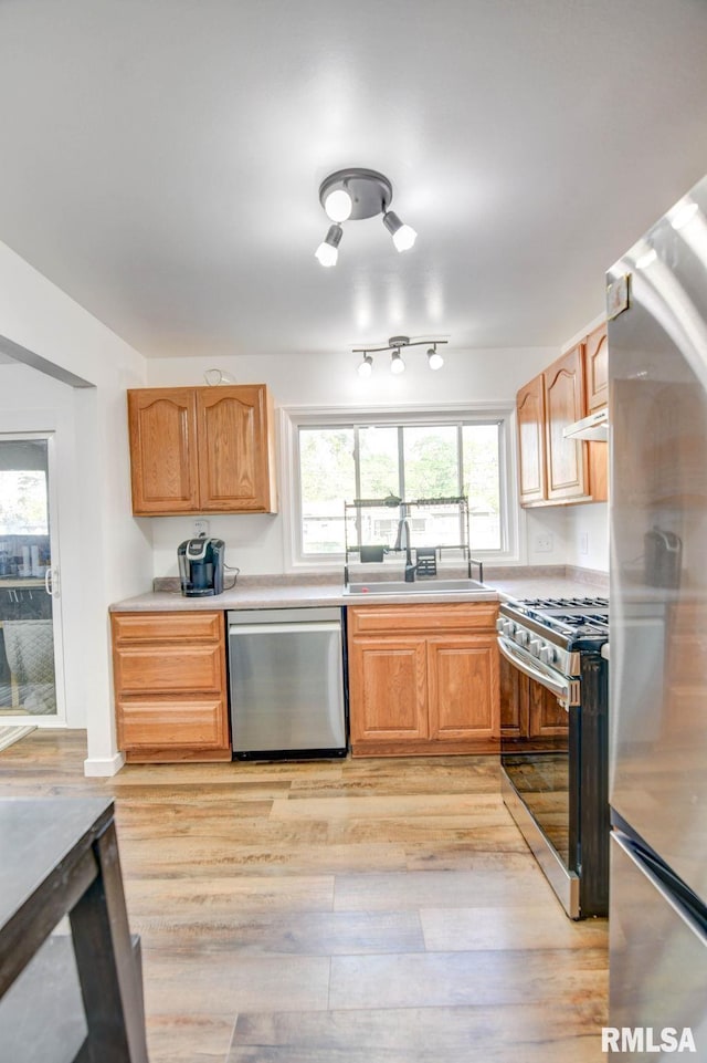 kitchen with appliances with stainless steel finishes, a sink, light wood finished floors, light countertops, and under cabinet range hood