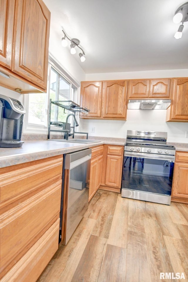 kitchen featuring a sink, light countertops, stainless steel appliances, light wood-type flooring, and under cabinet range hood