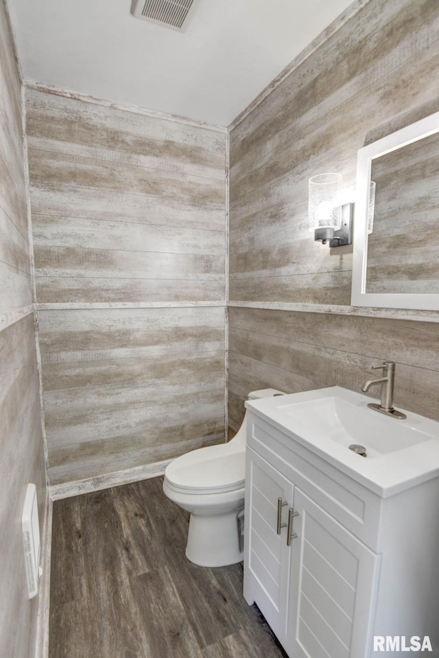 bathroom with visible vents, wood finished floors, vanity, toilet, and wooden walls