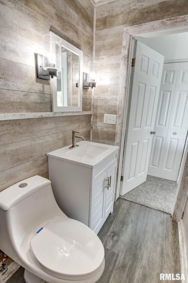 bathroom featuring toilet, wood walls, wood finished floors, and vanity