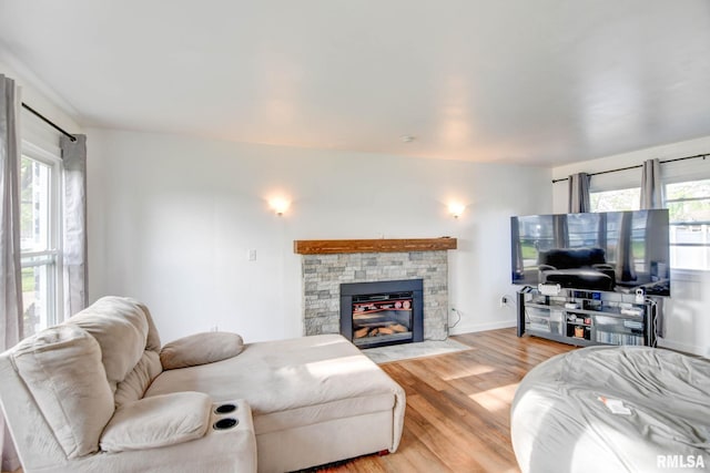 living room featuring baseboards, a stone fireplace, a healthy amount of sunlight, and light wood finished floors
