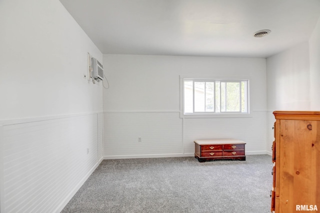 unfurnished bedroom featuring an AC wall unit, carpet, a wainscoted wall, and visible vents