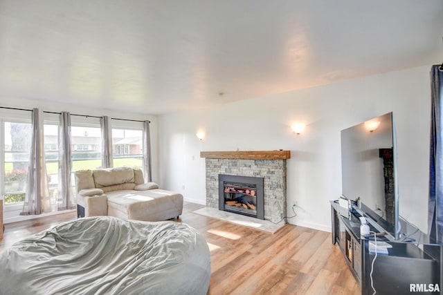 living area with baseboards, a stone fireplace, and light wood finished floors