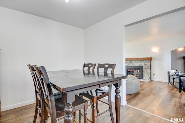 dining space featuring baseboards, a stone fireplace, and wood finished floors
