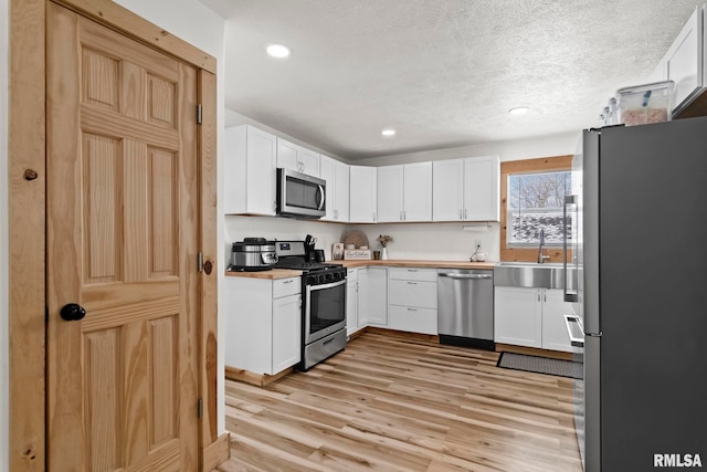 kitchen featuring light wood-type flooring, stainless steel appliances, a textured ceiling, white cabinets, and sink