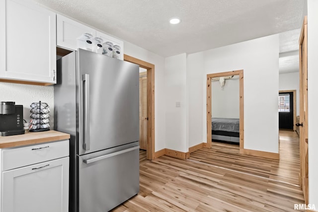 kitchen featuring butcher block countertops, light hardwood / wood-style flooring, stainless steel refrigerator, a textured ceiling, and white cabinets