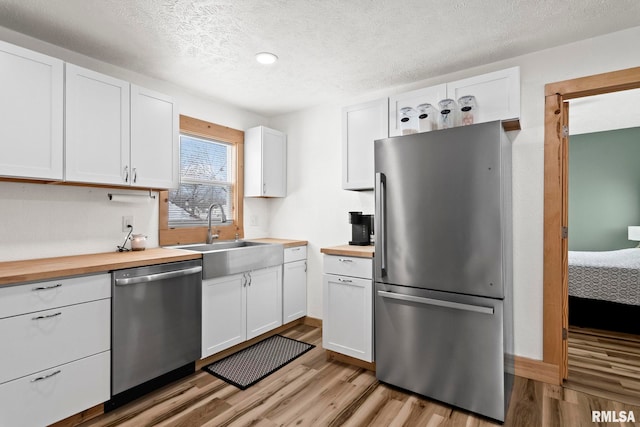 kitchen featuring white cabinetry, stainless steel appliances, light hardwood / wood-style floors, sink, and wooden counters