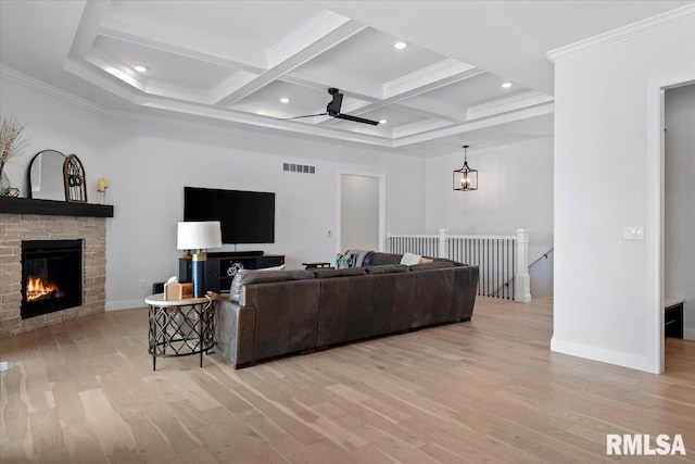 living room with crown molding, light wood finished floors, a stone fireplace, beamed ceiling, and visible vents