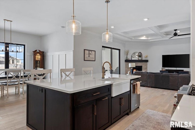 kitchen featuring a kitchen island with sink, dishwasher, a sink, light countertops, and coffered ceiling