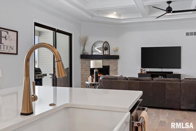 room details featuring visible vents, ornamental molding, beam ceiling, a lit fireplace, and a sink